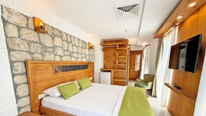 Un dormitorio con pared de piedra, cama de madera, almohadas verdes, un televisor y un armario de madera.