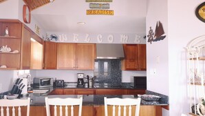 Cozinha com armários de madeira, bancada de granito, micro-ondas, torradeira e cafeteira. Há um letreiro com a palavra 'WELCOME' na parede e uma decoração de navio acima dos armários.