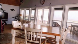 Uma área de refeições com mesa de madeira e cadeiras brancas, um telescópio e uma televisão.