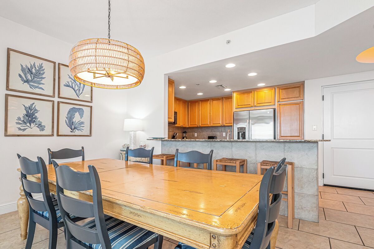 Uma sala de jantar com mesa e cadeiras de madeira, luminária pendente e uma cozinha com armários de madeira e uma geladeira.