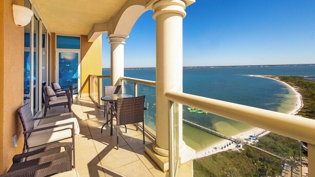 Ein Balkon mit Korbmöbeln, einem Tisch und Blick aufs Meer.