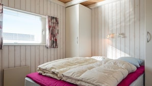 A bedroom with a bed, a window with blinds, a radiator, and a wall-mounted light fixture.