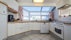 A compact kitchen with white cabinets, a dishwasher, a stove, and a window with blinds.