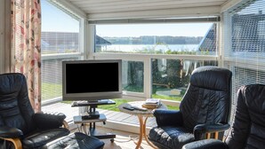 A sunroom with a large TV, two leather chairs, and a small table with a remote control.