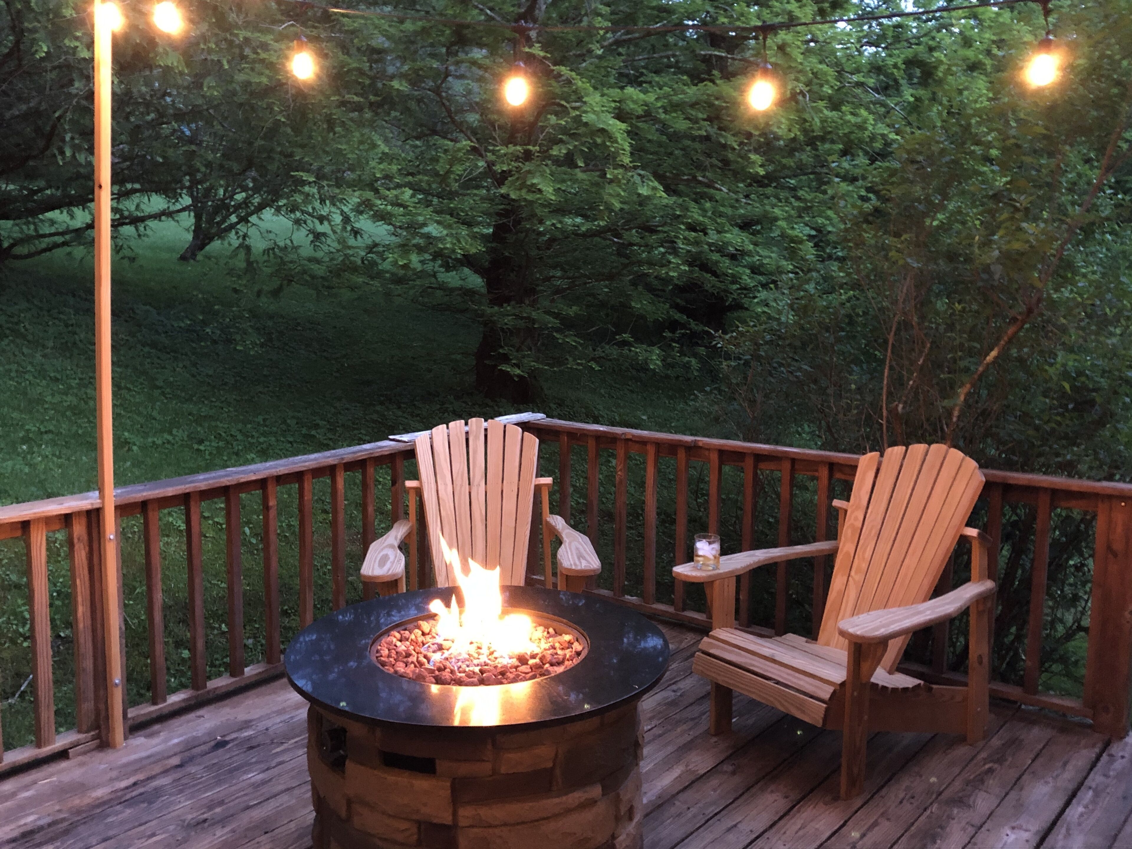 A wooden deck with a circular fire pit and two Adirondack chairs.