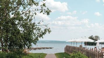 A paved pathway leading to a waterfront area with a wooden fence and umbrellas.