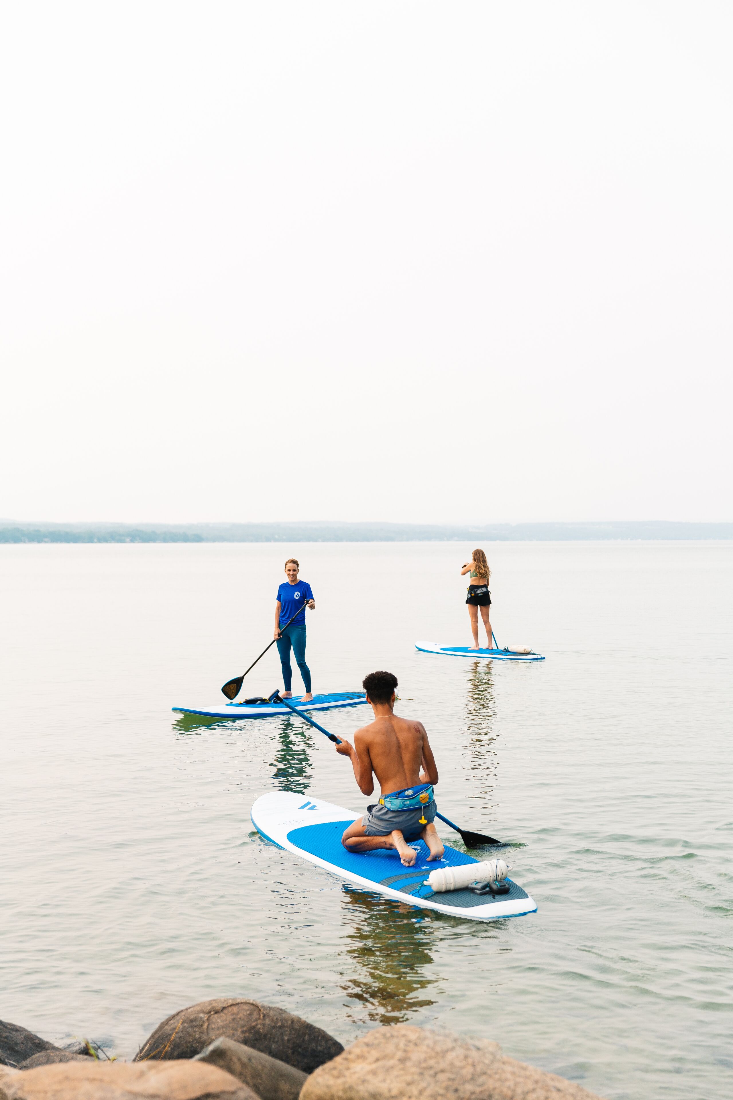 Tres personas en tablas de remo sobre aguas tranquilas.