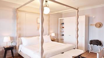 A four-poster bed with a canopy, bedside tables with lamps, a bedside shelf, a wardrobe, and a suitcase on a chair.