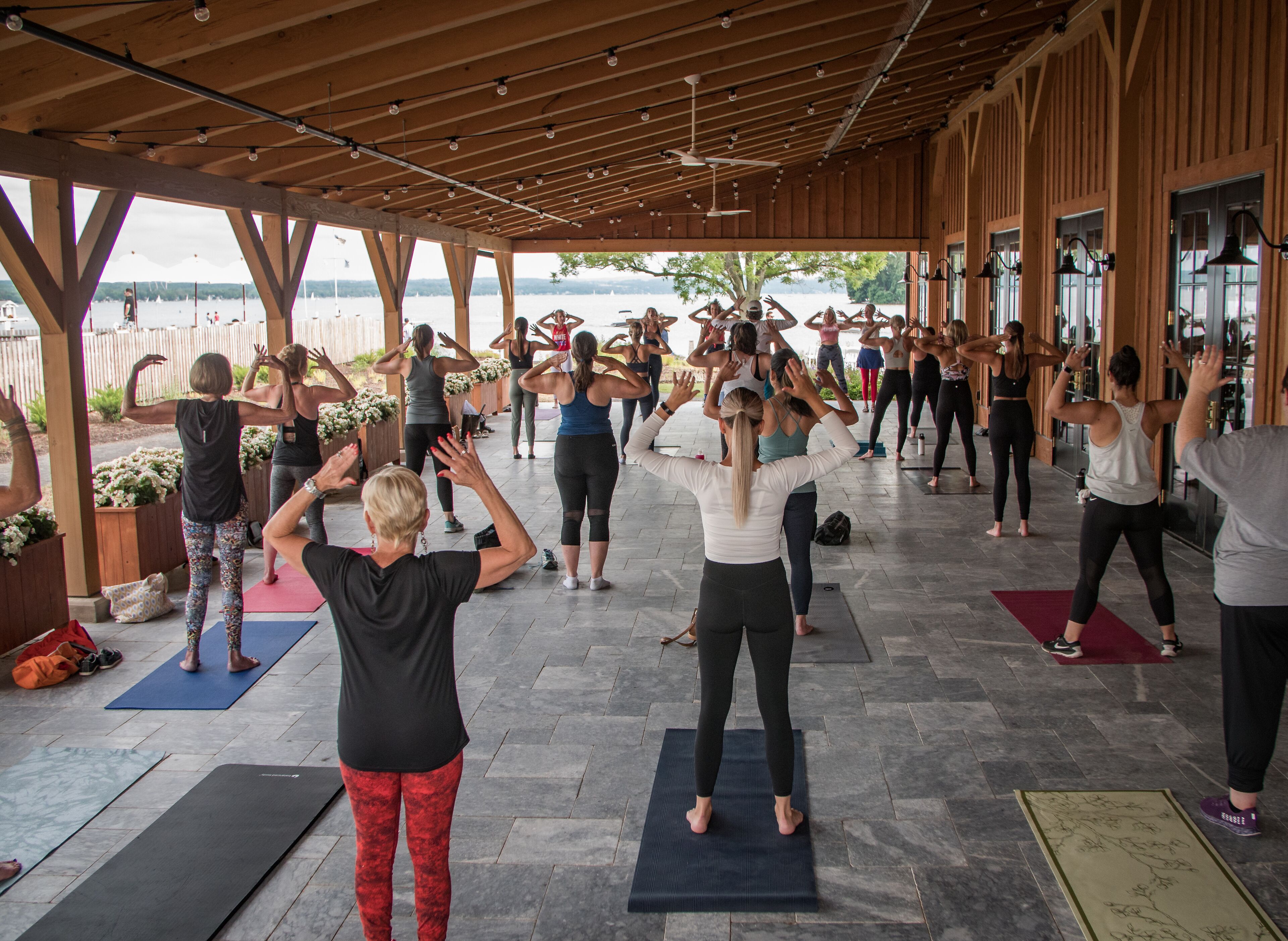 A group of people performing yoga in a covered outdoor area with a view of the water.