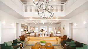 A spacious living room with a high ceiling, a central sofa, and multiple green armchairs.