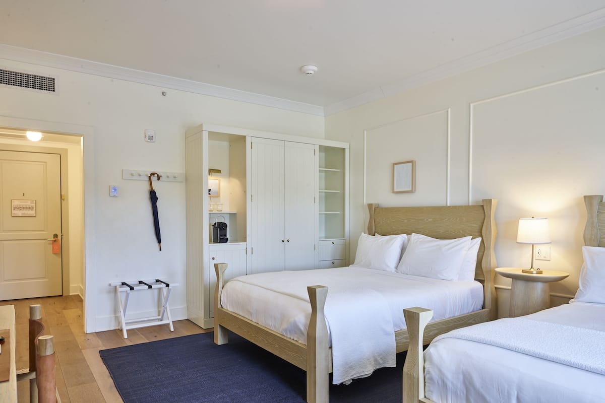 Ein Hotelzimmer mit zwei Betten, einem Kleiderschrank, einem Spiegel, einer Lampe und einem Kleiderhaken.