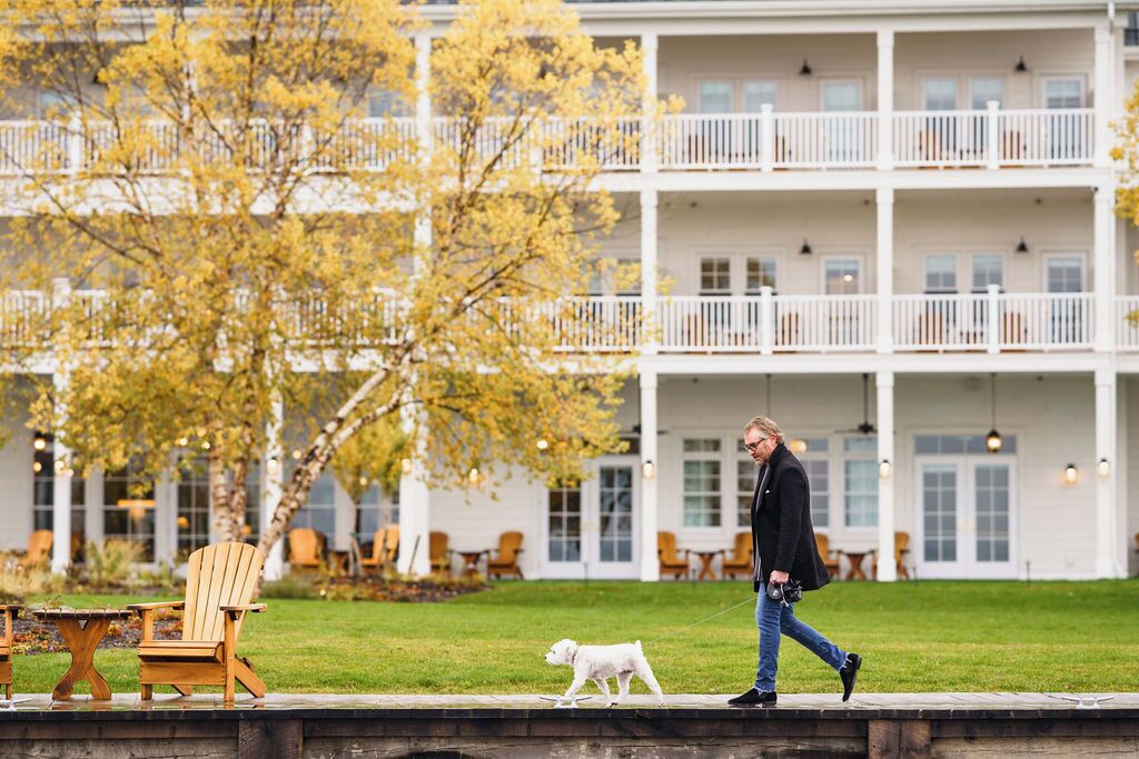 A person walking a dog on a grassy area in front of a building with multiple balconies and outdoor seating.