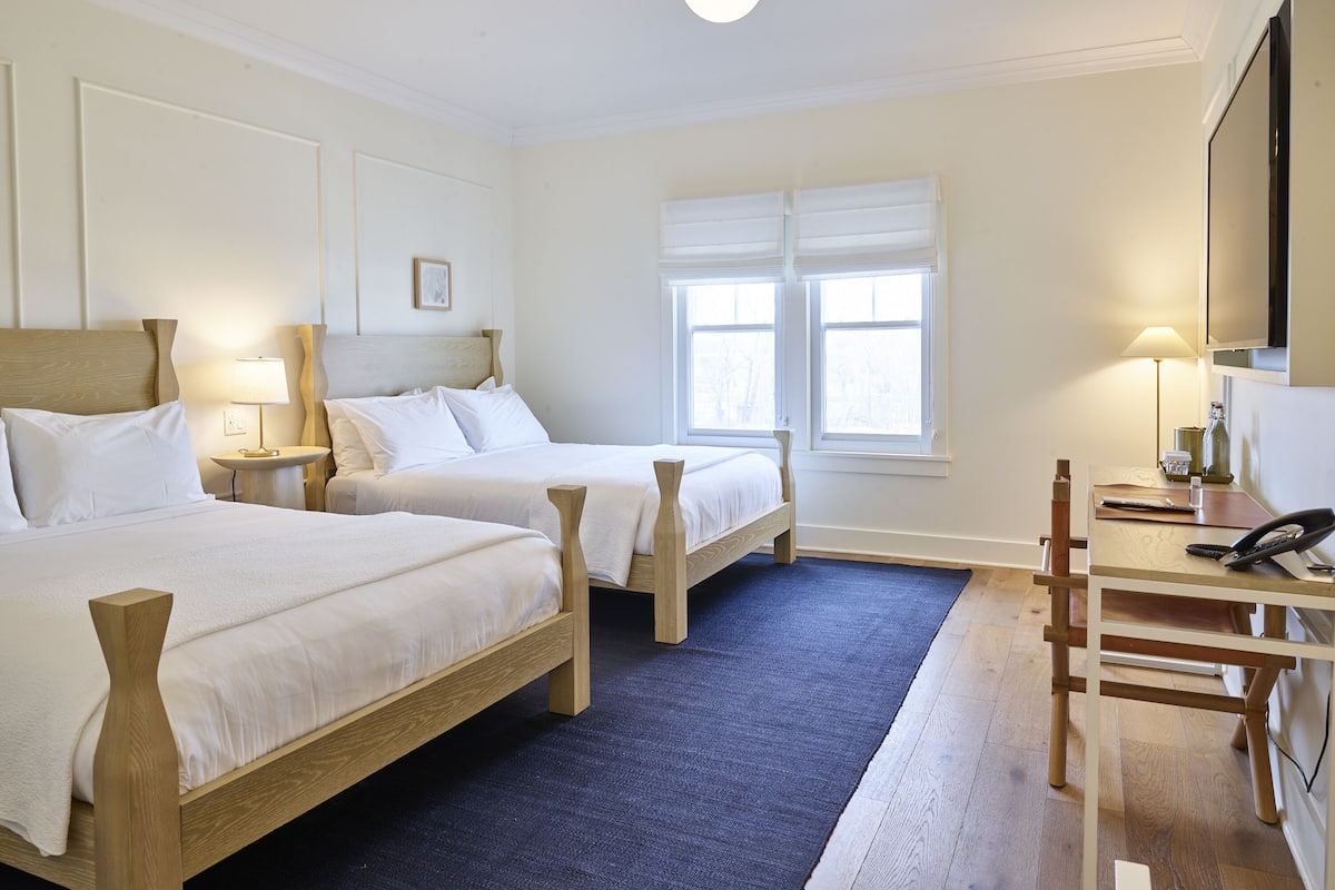 Ein Hotelzimmer mit zwei Betten, einem Schreibtisch und einem Stuhl.