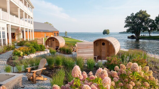 A spa area with wooden tubs, a lounge chair, and a building with a balcony overlooking a lake.