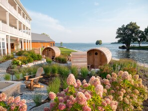 Een wellnessruimte met houten baden, een lounge stoel en een gebouw met balkon met uitzicht op een meer.