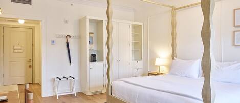 Una cama con dosel de madera, una mesita de noche con lámpara, un armario y una pequeña zona de estar con una silla y una mesa.