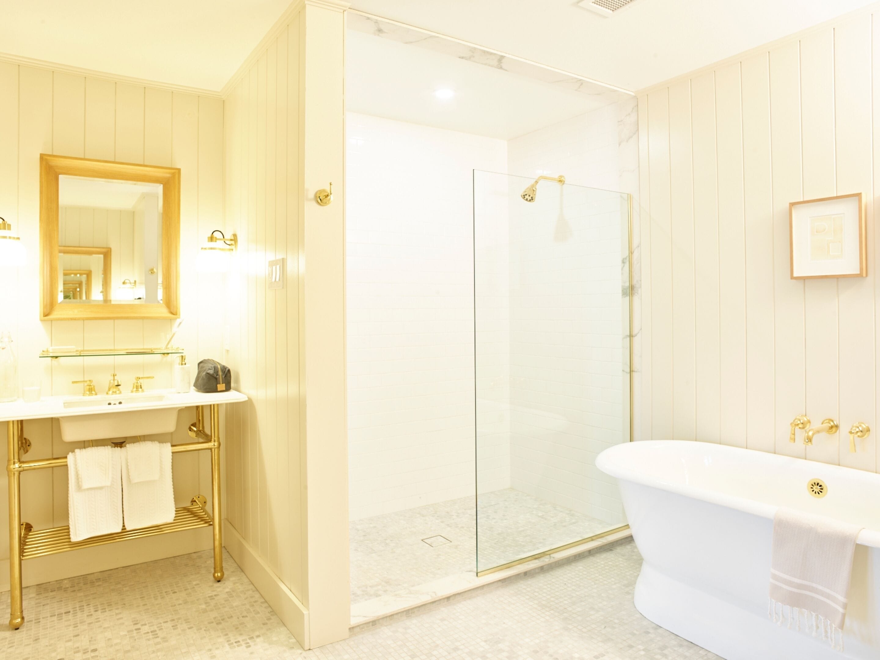 A bathroom with a white sink, gold fixtures, a glass shower enclosure, and a freestanding bathtub.