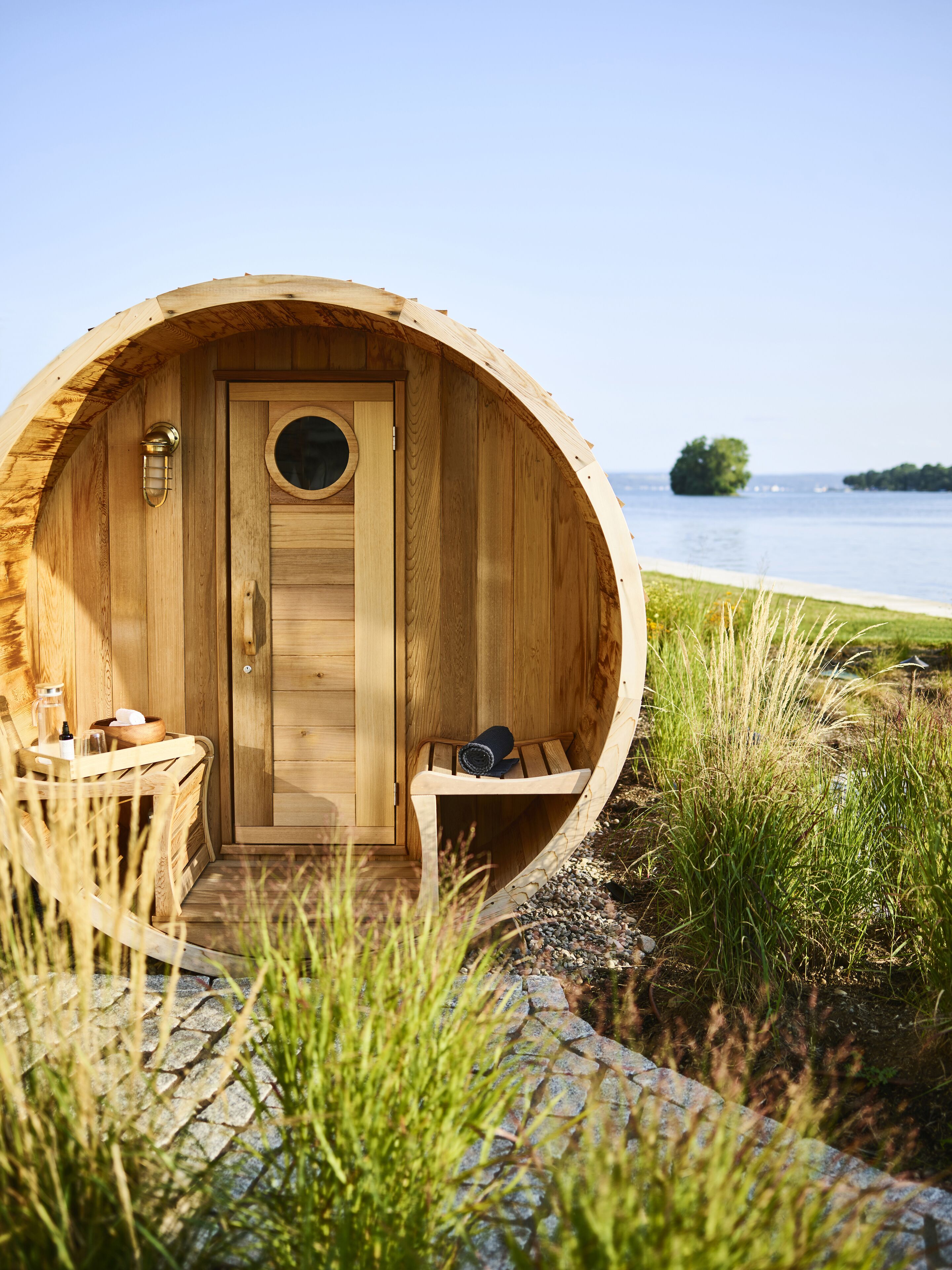 A wooden cabin with a circular door, a small seating area with a bench, and a table with a glass and a bottle.
