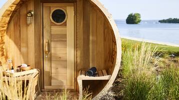 A wooden cabin with a circular door, a small seating area with a bench, and a table with a glass and a bottle.