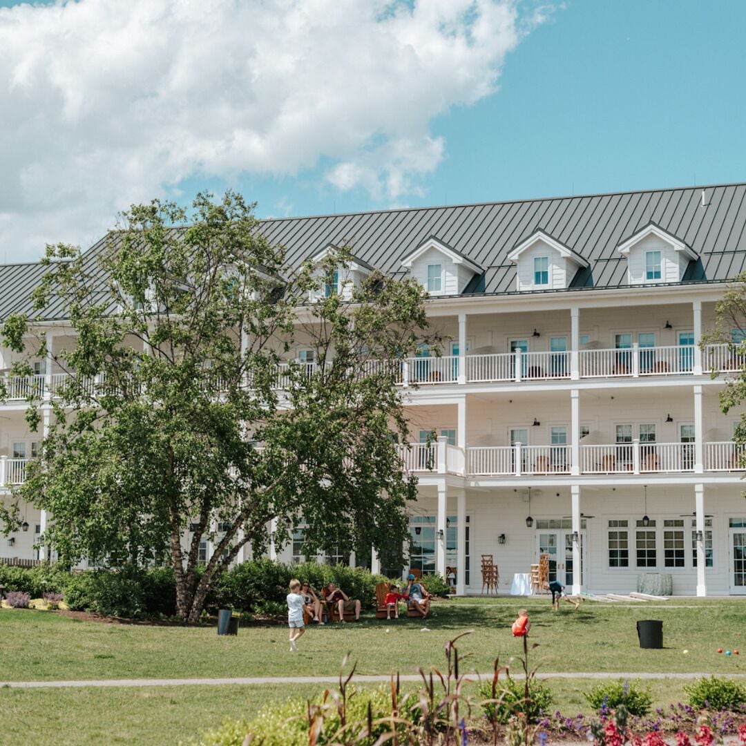 A multi-story hotel with a white facade, balconies, and a grassy courtyard.