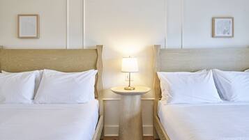 A hotel room with two beds, a round bedside table with a lamp, and two framed artworks on the walls.