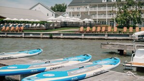 A waterfront hotel with a pool area, lounge chairs, and paddleboards docked at the pier.