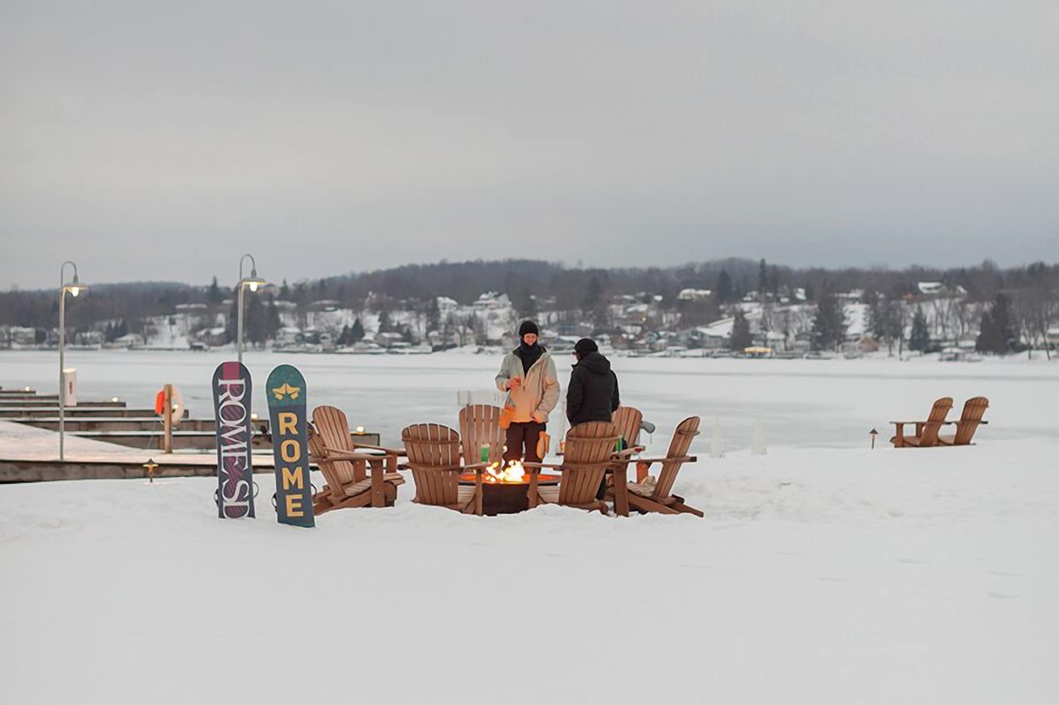 A snow-covered beach with wooden chairs and a fire pit, and two signs reading "ROME" and "ROME'S".