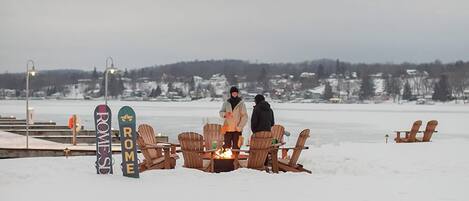 A snow-covered beach with wooden chairs and a fire pit, and two signs reading "ROME" and "ROME'S".
