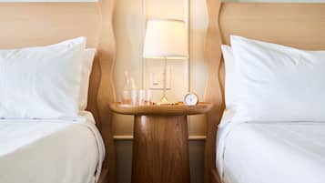 A hotel room with two beds, a wooden nightstand, a lamp, and a clock.