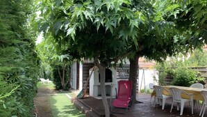 Eine Holzterrasse mit Tisch und Stühlen, umgeben von üppigem Grün und einem Baum.