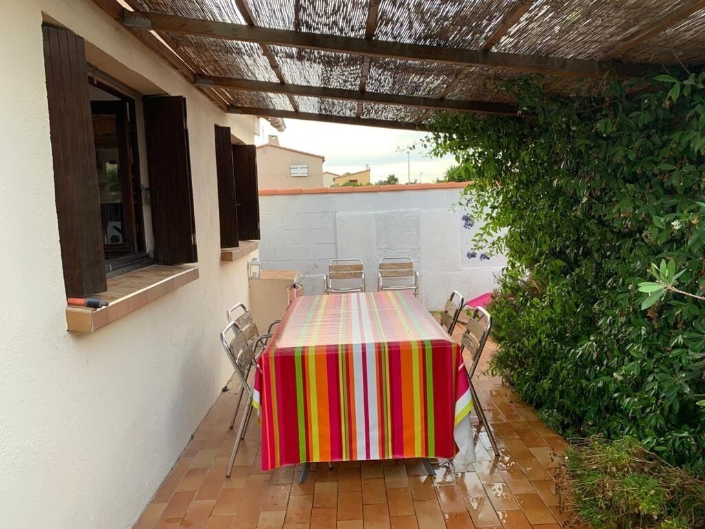 Une terrasse extérieure avec une table et des chaises, un espace abrité et un mur recouvert de plantes grimpantes.