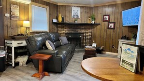 A cabin-style interior with a fireplace, leather sofa, wooden flooring, and a television. - Pet-Friendly Sleepin Inn Cabin w/ Hot Tub & Fireplace (Ruidoso)