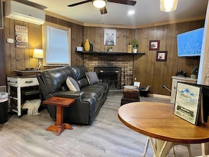 A cabin-style interior with a fireplace, leather sofa, wooden flooring, and a television. - Pet-Friendly Sleepin Inn Cabin w/ Hot Tub & Fireplace (Ruidoso)