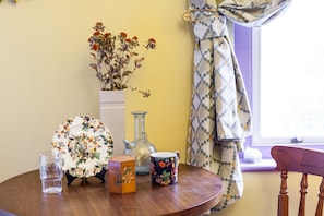 A table in a cozy room features a vase with dried flowers, a plate, a tumbler, and a mug.