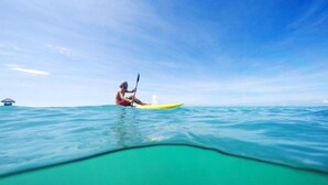 Eine Person paddelt mit einem Kajak auf türkisblauem Wasser unter einem wolkenlosen Himmel.