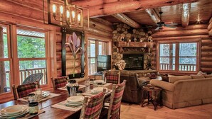 A rustic cabin interior with a dining area, a fireplace, and a cozy living room.
