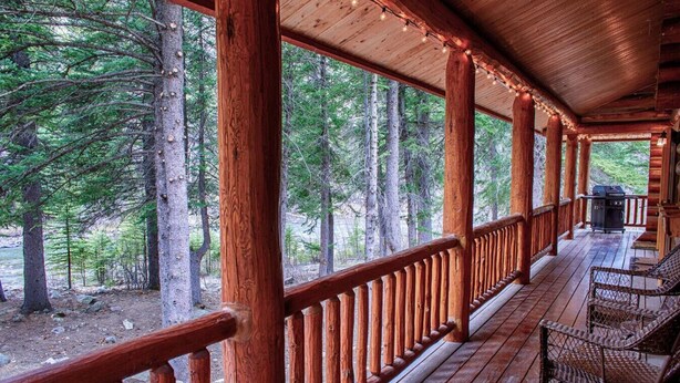 A wooden deck with a railing, surrounded by trees, and a grill on the deck.