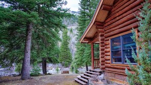 A log cabin with a porch, a bench, and a view of a forested mountain.