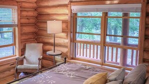 A log cabin bedroom with a bed, a chair, a lamp, and a ceiling fan.