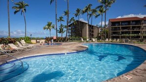 A swimming pool with lounge chairs, palm trees, and a hotel building in the background. - Papakea Paradise, G102, 2 Bedroom & 2 Bathroom, Ground Level, Air Con, Specials! (Lahaina)
