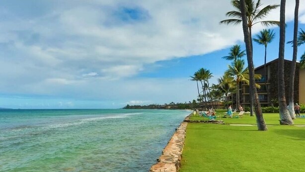 A beachfront hotel with a stone wall, palm trees, and a clear view of the ocean. - Papakea Paradise, G102, 2 Bedroom & 2 Bathroom, Ground Level, Air Con, Specials! (Lahaina)