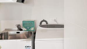 Cocina compacta con un lavamanos de acero inoxidable, una lavadora y una pared blanca con toma de corriente.