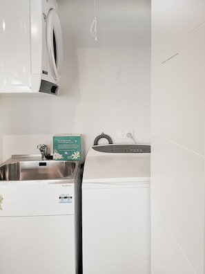 A compact kitchen with a stainless steel sink, a washing machine, and a white wall with a power outlet.