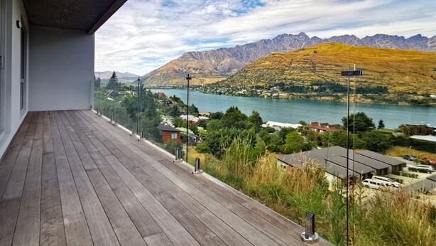 Una terraza de madera con vistas a un lago, montañas y un pueblo pequeño.