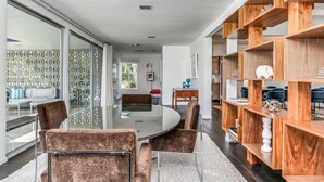 Un comedor moderno con una mesa de vidrio y sillas acolchadas, una estantería de madera y vistas a través de un panel de vidrio.