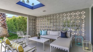 Un área de estar exterior moderna con un sofá blanco, sillas y una mesa de centro.