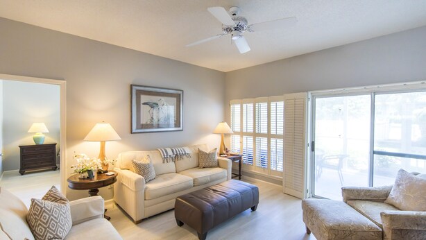 A spacious living room with a beige sofa, a brown ottoman, and a patterned armchair. There are two side tables with lamps and a framed artwork on the wall. - Deeded Beach Access, Community Pool, Screen Porch, Walk to Shops and Restaurants (Santa Rosa Beach)