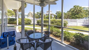 A covered outdoor area with a glass table and chairs, a ceiling fan, and a view of a white picket fence and greenery. - Deeded Beach Access, Community Pool, Screen Porch, Walk to Shops and Restaurants (Santa Rosa Beach)