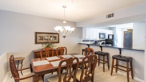 A dining area with a wooden table and chairs, a chandelier, and a kitchen in the background. - Deeded Beach Access, Community Pool, Screen Porch, Walk to Shops and Restaurants (Santa Rosa Beach)