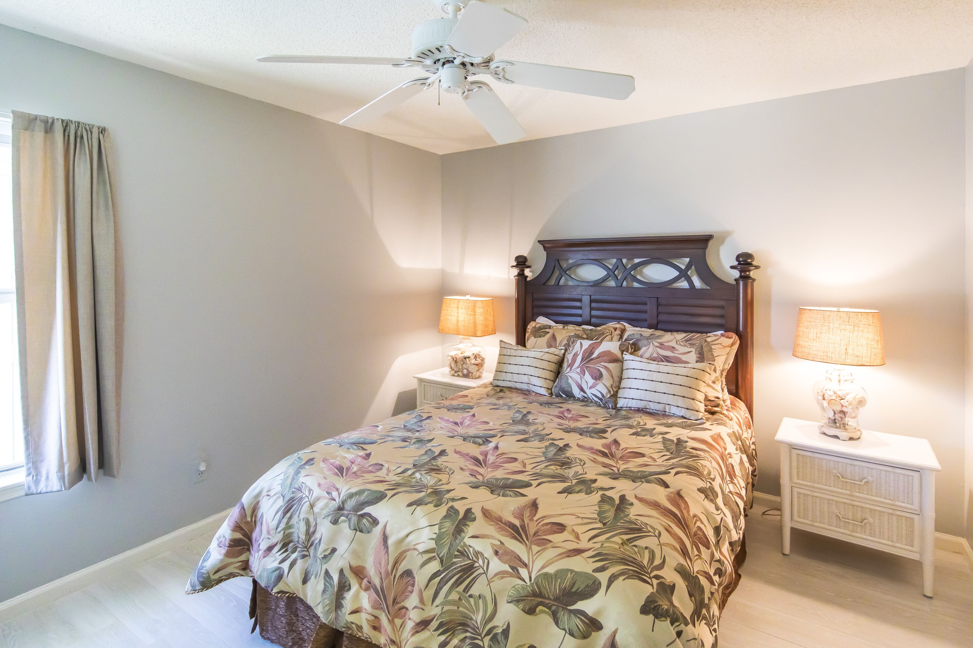 A bedroom with a bed, nightstands, lamps, a ceiling fan, and a window with curtains.
